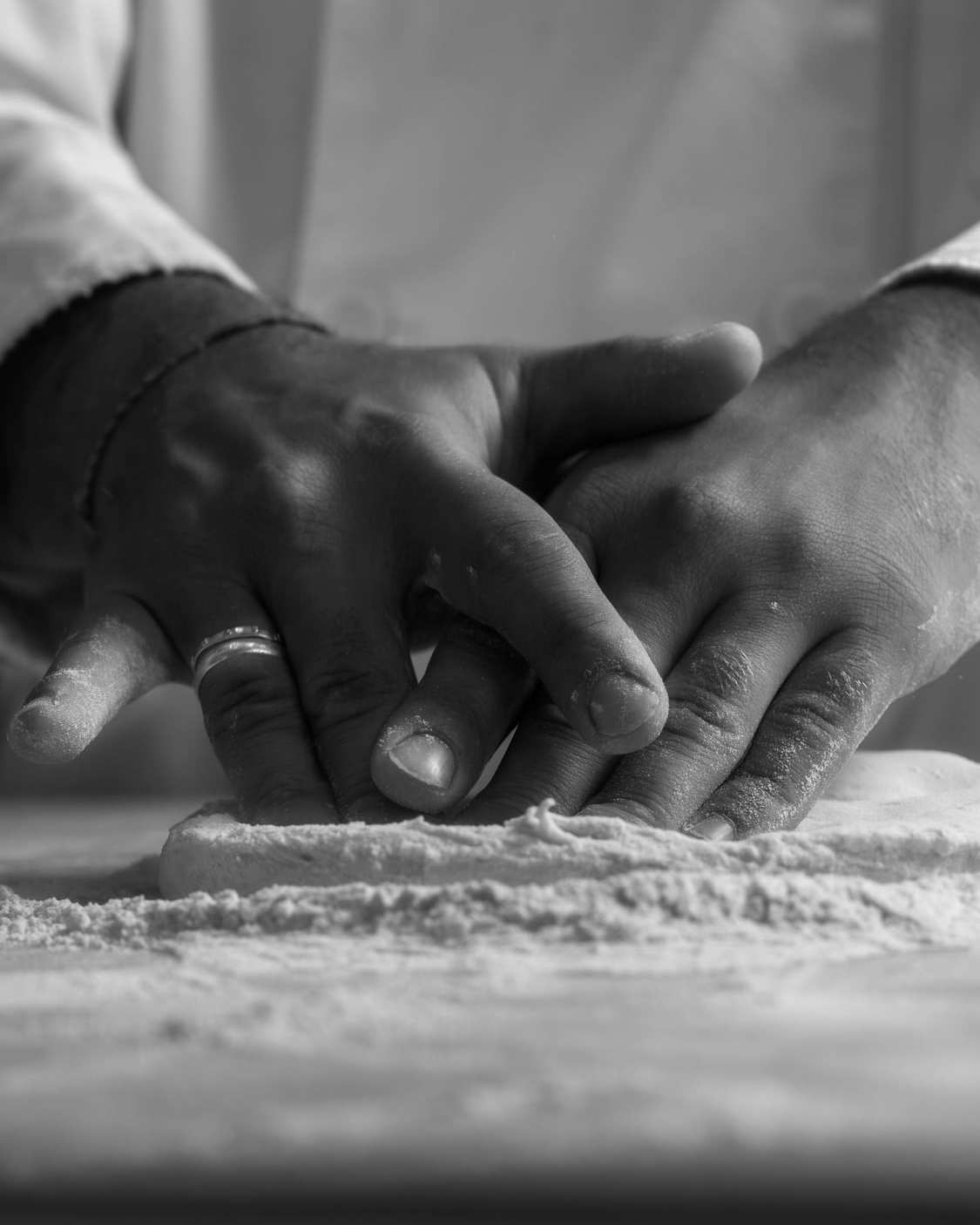 Manos con harina trabajan una masa sobre la mesa, en blanco y negro.