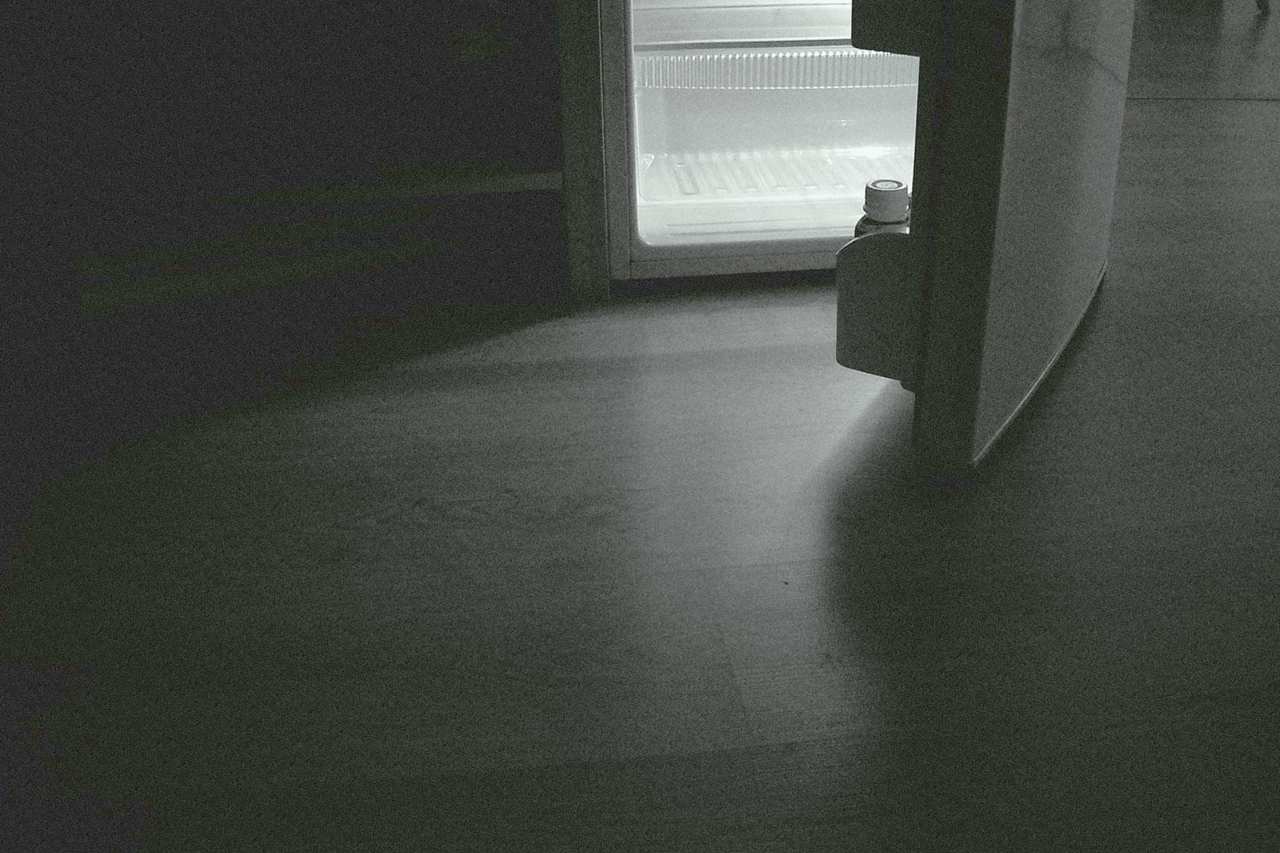 Frigorífico con la puerta entreabierta y la luz encendida en una habitación a oscuras.