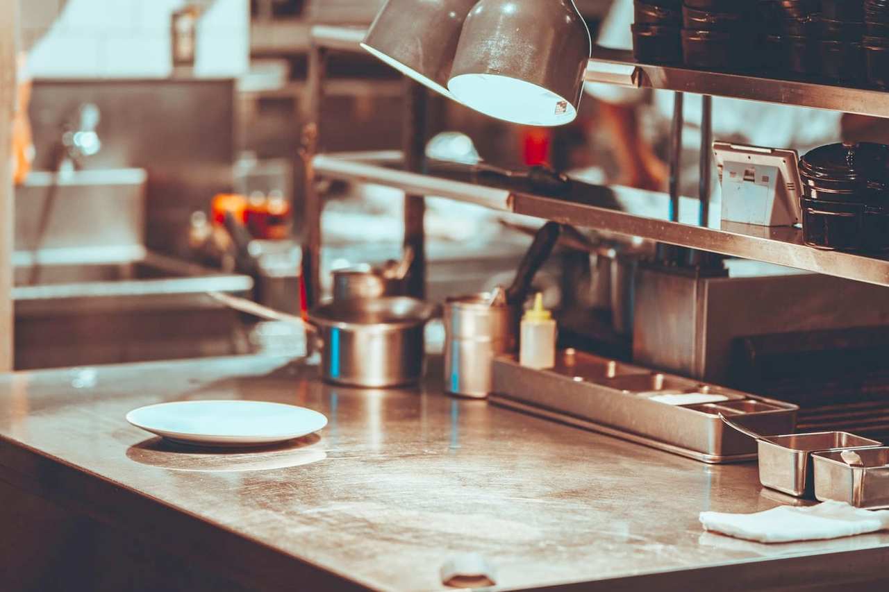 Lámparas de calor sobre el pase de una cocina, con un plato vacío en la mesa de acero.