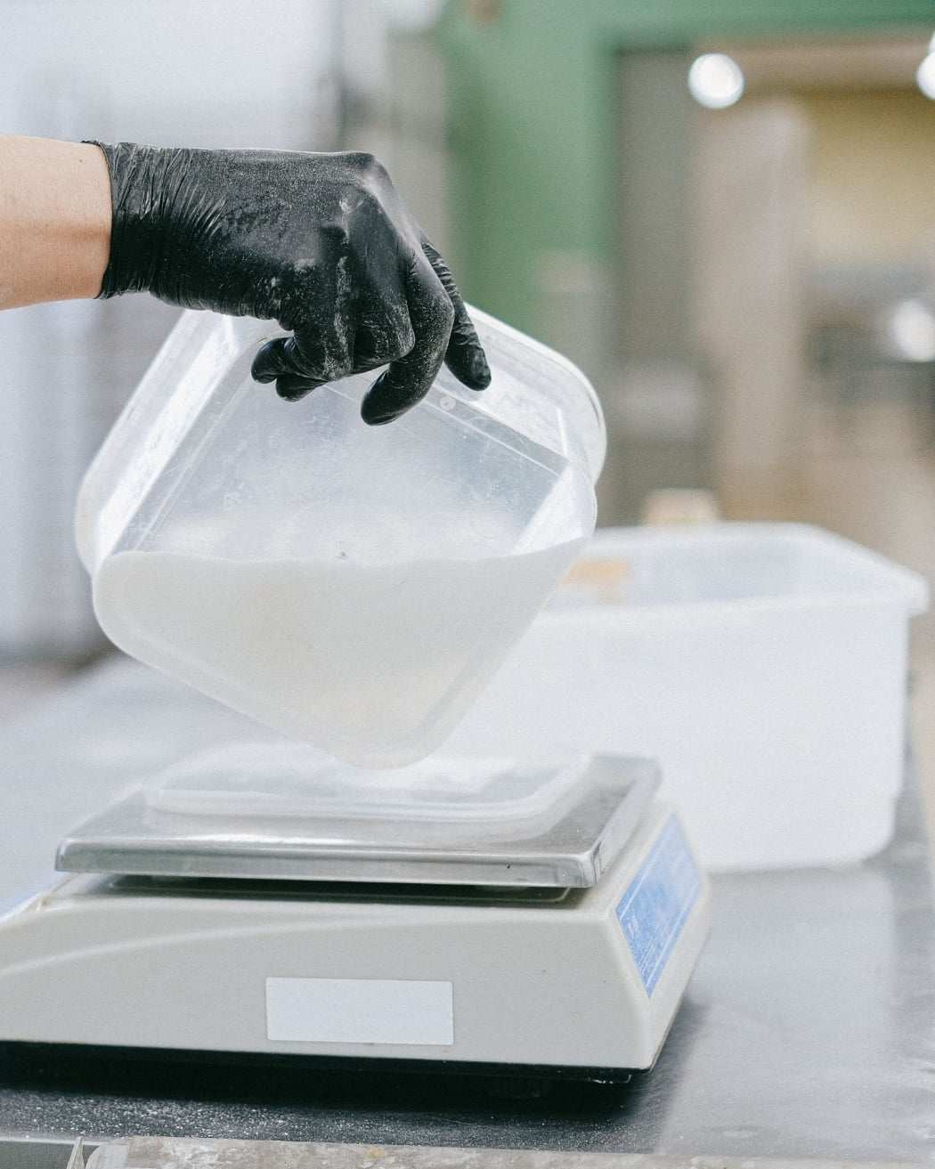 Mano con guante negro vierte un ingrediente blanco en una báscula de cocina.