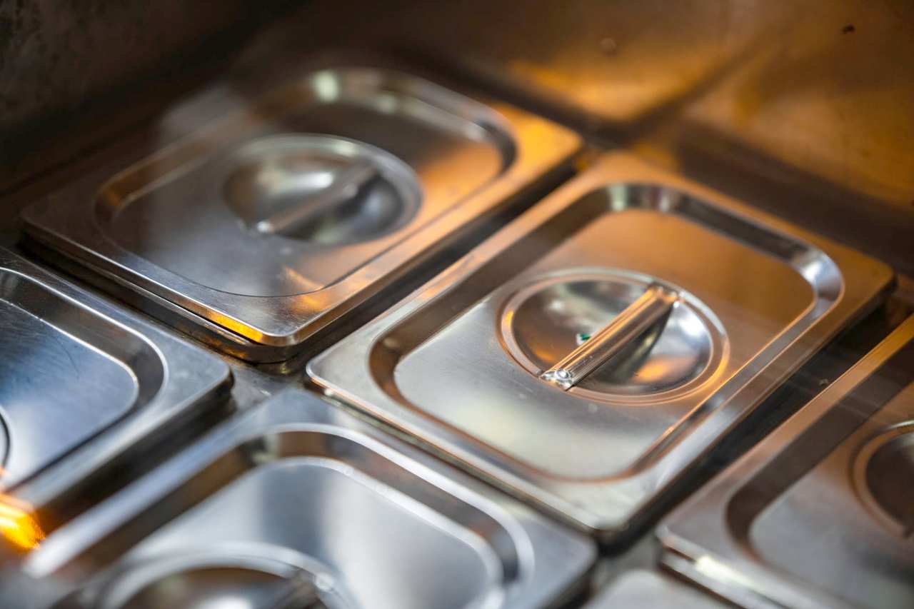Tapas de acero inoxidable de recipientes de cocina, alineadas y con un reflejo anaranjado.
